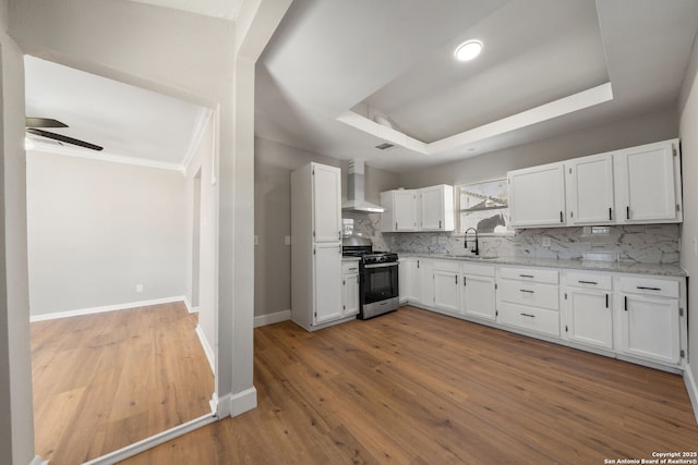 kitchen with a sink, a tray ceiling, tasteful backsplash, gas stove, and wall chimney exhaust hood
