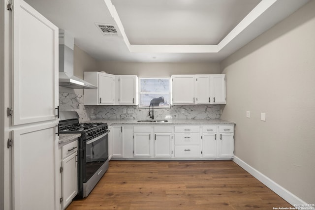 kitchen with black gas range, wall chimney exhaust hood, white cabinets, and a sink