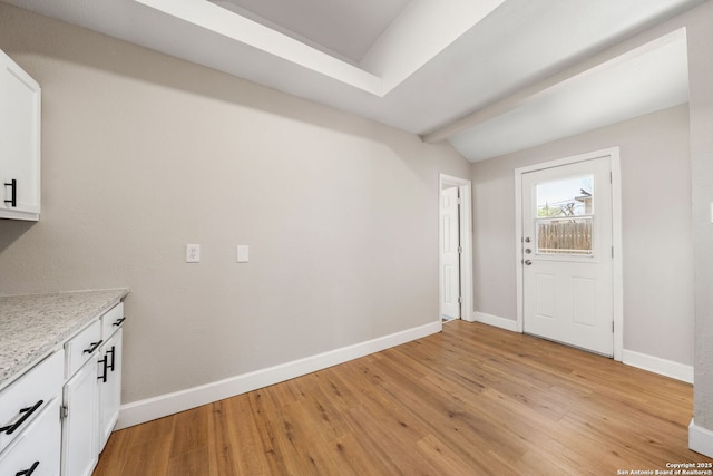 interior space with baseboards, lofted ceiling with beams, and light wood-style floors