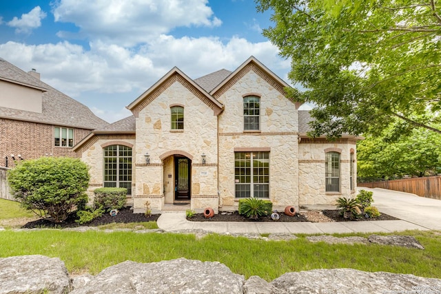 french country home with fence, roof with shingles, and stone siding