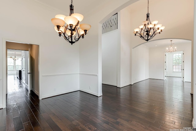 spare room with dark wood-style flooring, arched walkways, baseboards, and a notable chandelier