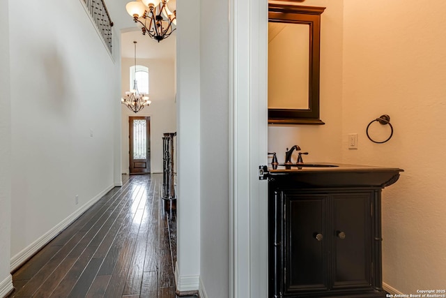 corridor with baseboards, an inviting chandelier, dark wood finished floors, and a towering ceiling