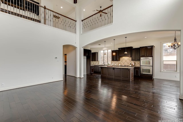 unfurnished living room with an inviting chandelier, arched walkways, a high ceiling, and dark wood-type flooring