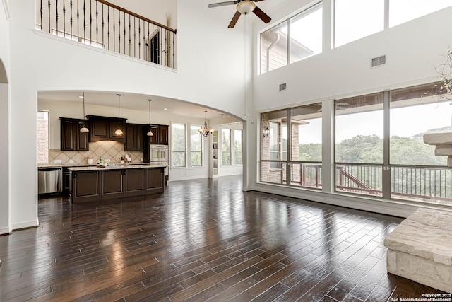 living room featuring a high ceiling, ceiling fan with notable chandelier, dark wood-style flooring, and visible vents