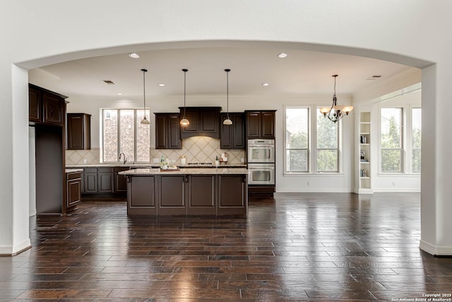 kitchen featuring arched walkways, appliances with stainless steel finishes, dark wood finished floors, dark brown cabinets, and a chandelier