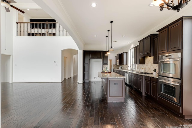 kitchen with arched walkways, appliances with stainless steel finishes, dark brown cabinets, and ornamental molding