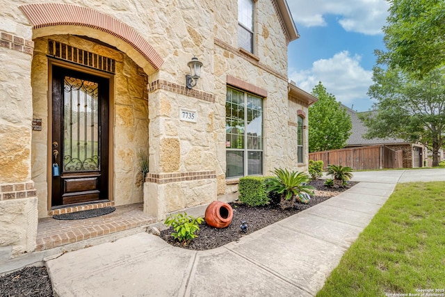 view of exterior entry featuring fence and stone siding
