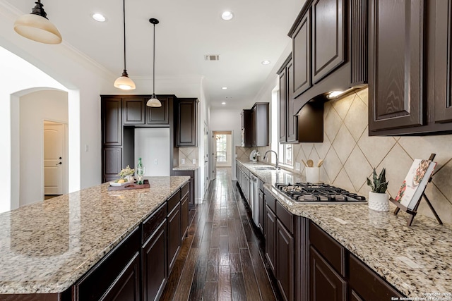 kitchen featuring dark brown cabinetry, light stone counters, a sink, stainless steel gas stovetop, and visible vents