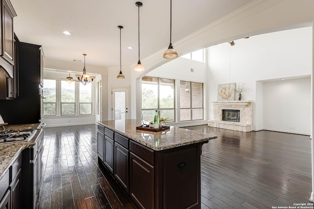 kitchen featuring an inviting chandelier, a stone fireplace, open floor plan, dark wood-style floors, and stainless steel gas stovetop