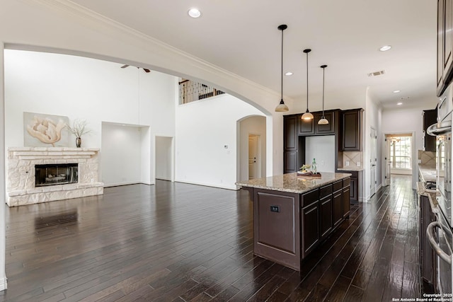 kitchen with visible vents, arched walkways, dark brown cabinetry, and a kitchen island