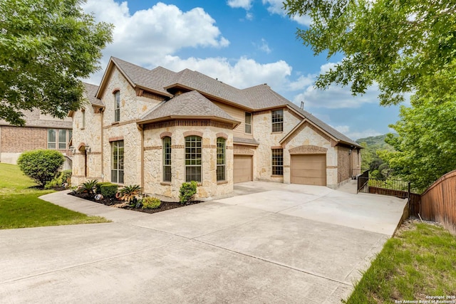 french provincial home featuring driveway, a garage, fence, a shingled roof, and stone siding