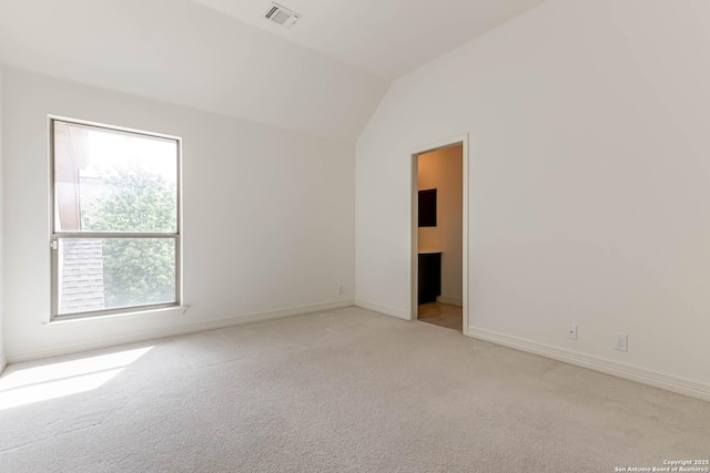 spare room featuring a wealth of natural light, carpet flooring, lofted ceiling, and visible vents