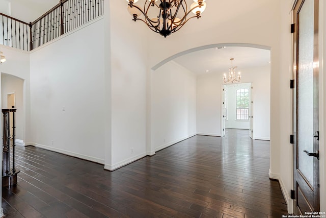 interior space featuring arched walkways, a notable chandelier, dark wood-style floors, and a towering ceiling