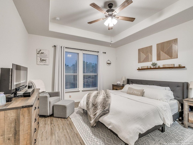 bedroom featuring a ceiling fan, a raised ceiling, and light wood-style flooring
