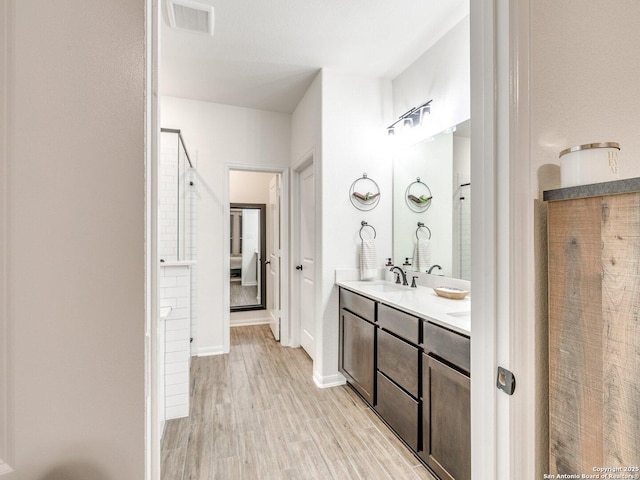 bathroom featuring a sink, wood finished floors, baseboards, visible vents, and double vanity