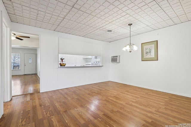 unfurnished dining area with ceiling fan with notable chandelier, baseboards, and wood finished floors