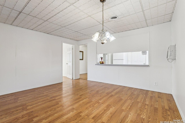 unfurnished living room with a notable chandelier, wood finished floors, visible vents, and baseboards