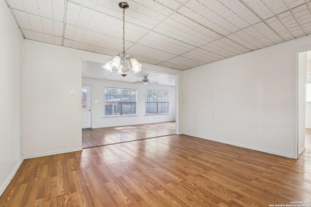unfurnished dining area featuring ceiling fan with notable chandelier, wood finished floors, and baseboards
