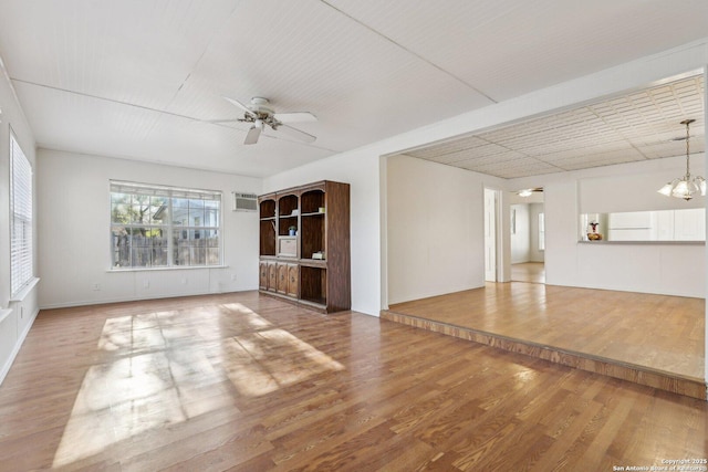 unfurnished living room with ceiling fan with notable chandelier, a wall mounted air conditioner, and wood finished floors