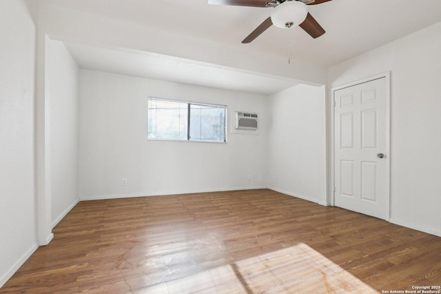 unfurnished bedroom featuring baseboards, wood finished floors, a ceiling fan, and a wall unit AC