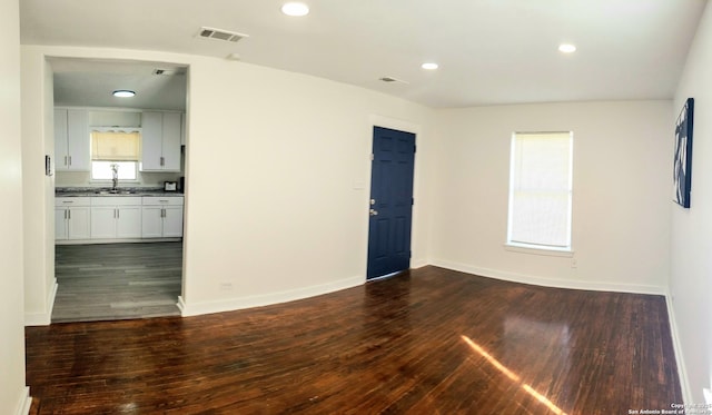 unfurnished room with visible vents, a sink, recessed lighting, baseboards, and dark wood-style flooring