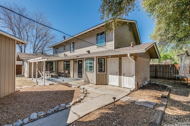 back of property featuring a trampoline, brick siding, fence, a patio, and a shingled roof