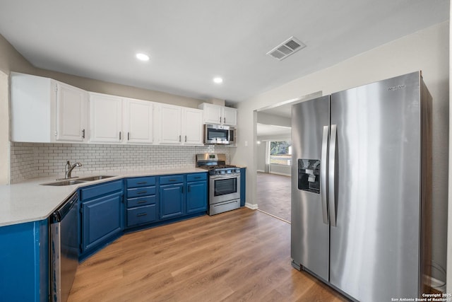 kitchen with blue cabinetry, white cabinets, appliances with stainless steel finishes, and a sink