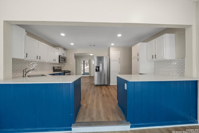 kitchen featuring light wood-style flooring, a sink, white cabinetry, appliances with stainless steel finishes, and a peninsula