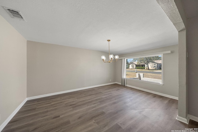 unfurnished dining area featuring dark wood finished floors, visible vents, a textured ceiling, and an inviting chandelier