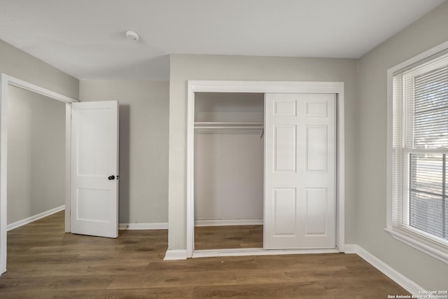 unfurnished bedroom featuring wood finished floors, baseboards, and a closet