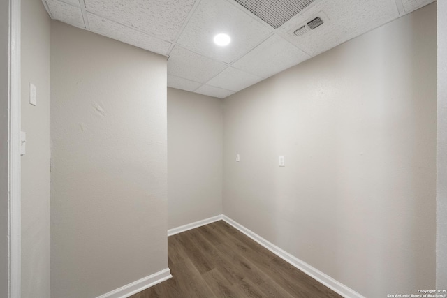 spare room with a paneled ceiling, visible vents, baseboards, and dark wood-type flooring