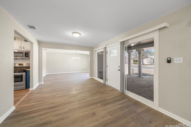 interior space with light wood-type flooring, visible vents, baseboards, and a notable chandelier