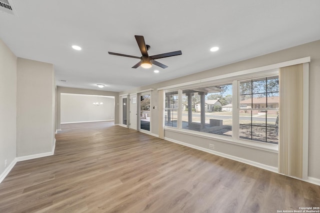 unfurnished room featuring wood finished floors, ceiling fan with notable chandelier, visible vents, and baseboards