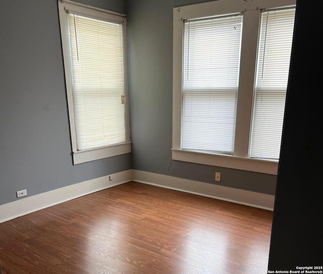 unfurnished room featuring wood finished floors, baseboards, and a wealth of natural light