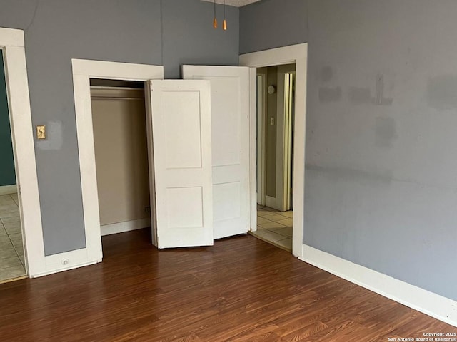 unfurnished bedroom featuring wood finished floors, a closet, and baseboards