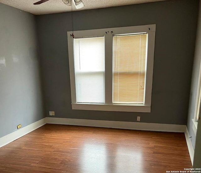 spare room with baseboards, a textured ceiling, wood finished floors, and a ceiling fan