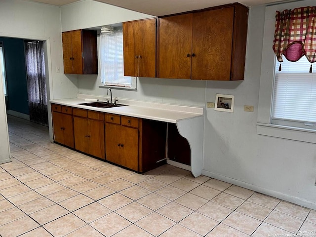 kitchen featuring a sink, baseboards, brown cabinetry, and light countertops