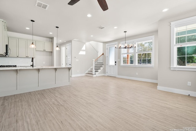 kitchen with visible vents, stainless steel microwave, a kitchen bar, light wood-type flooring, and ceiling fan with notable chandelier