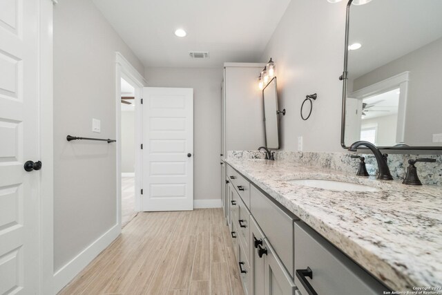 bathroom featuring wood finished floors, baseboards, double vanity, ceiling fan, and a sink