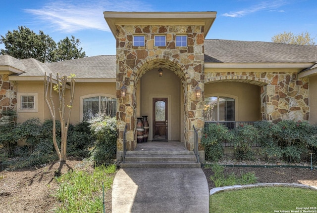 entrance to property featuring a shingled roof, stucco siding, and stone siding