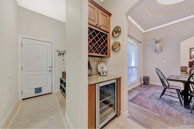 bar featuring crown molding, light wood finished floors, a bar, wine cooler, and arched walkways