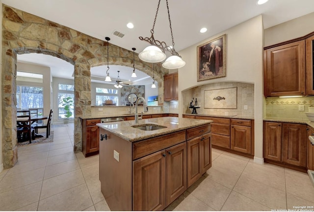 kitchen with arched walkways, a sink, tasteful backsplash, and a center island with sink