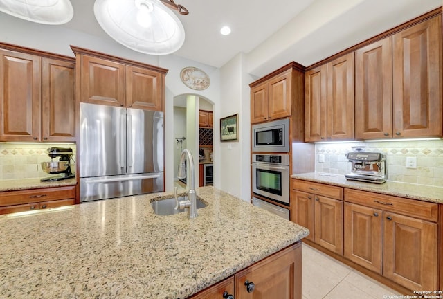 kitchen with tasteful backsplash, a sink, arched walkways, light stone counters, and appliances with stainless steel finishes
