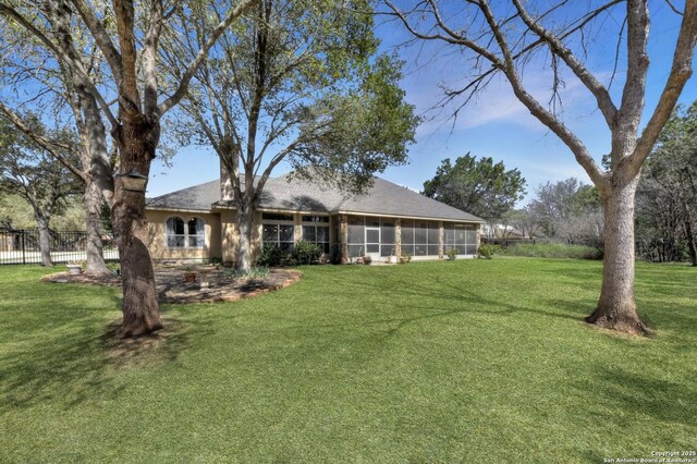 back of house featuring roof with shingles, a sunroom, fence, and a yard