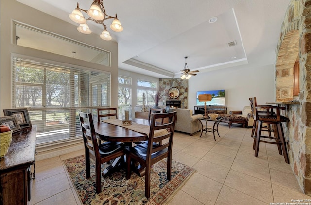 dining area featuring a raised ceiling, a fireplace, light tile patterned floors, ceiling fan with notable chandelier, and visible vents