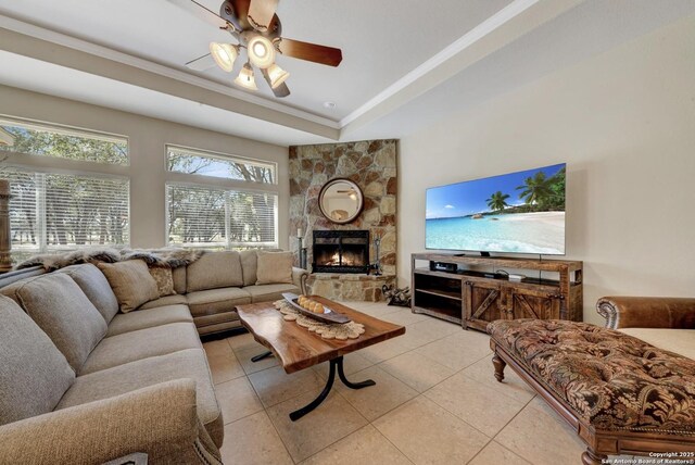 living room featuring a ceiling fan, a raised ceiling, light tile patterned floors, and a fireplace