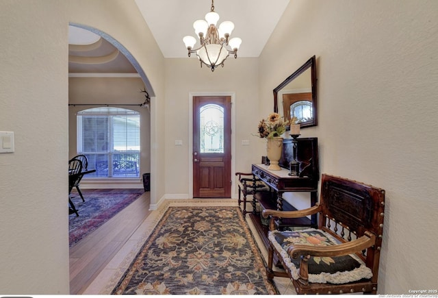 foyer featuring a chandelier, baseboards, wood finished floors, arched walkways, and vaulted ceiling