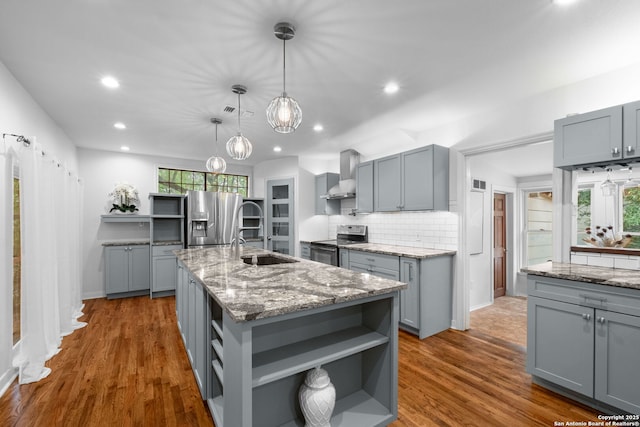 kitchen with open shelves, wall chimney range hood, gray cabinets, a sink, and appliances with stainless steel finishes