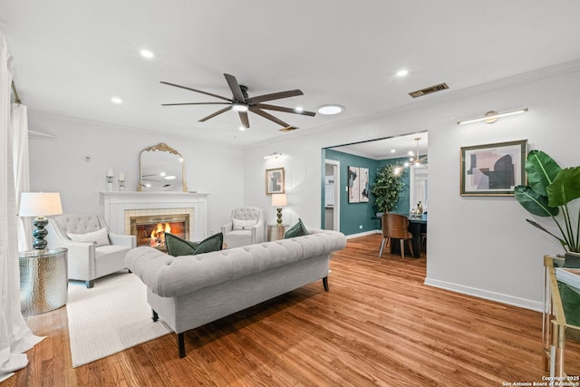 living area with visible vents, ornamental molding, light wood-style flooring, and a tile fireplace