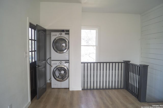 clothes washing area featuring stacked washer / dryer, laundry area, and wood finished floors